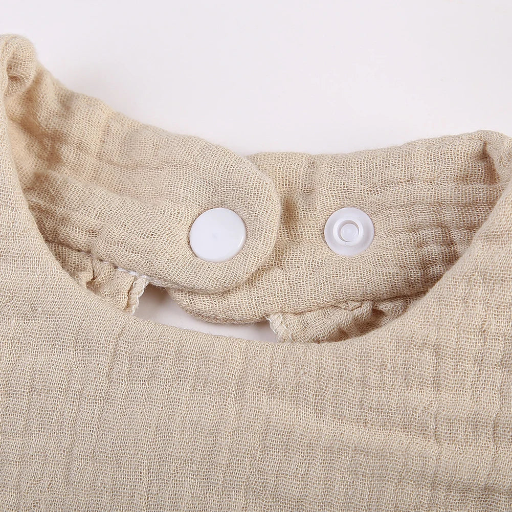 A close-up of a beige ruffled muslin cotton baby bib with an adjustable snap closure.