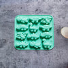 A silicone mold tray filled with green dinosaur shapes for baking, chocolate, and craft projects.