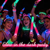 Group of young people celebrating in a dark party holding glowing LED foam sticks
