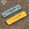 Two leather-style handmade with love tags, one blue and one yellow, are displayed on a brown textured background.