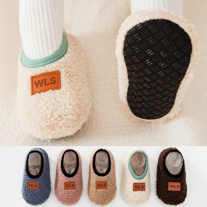A row of cozy plush baby slippers in various colors including gray, pink, beige, and brown with anti-slip soles.