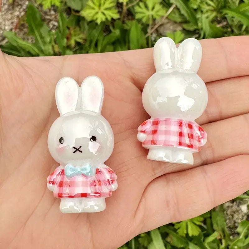 A white resin bead charm shaped like a rabbit with a pink checkered bow is held in a person's hand.