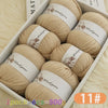 A box filled with 6 balls of beige wool yarn for knitting, showing the texture and packaging.