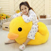 A young girl is sitting on a large yellow duck plush toy, smiling while wearing a white and blue patterned sweater.