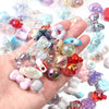 A hand holds a collection of colorful acrylic bow beads and various gemstone beads for DIY jewelry making.