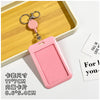 A pink rectangular ID badge holder with a keychain attached, displayed on a wooden tray.