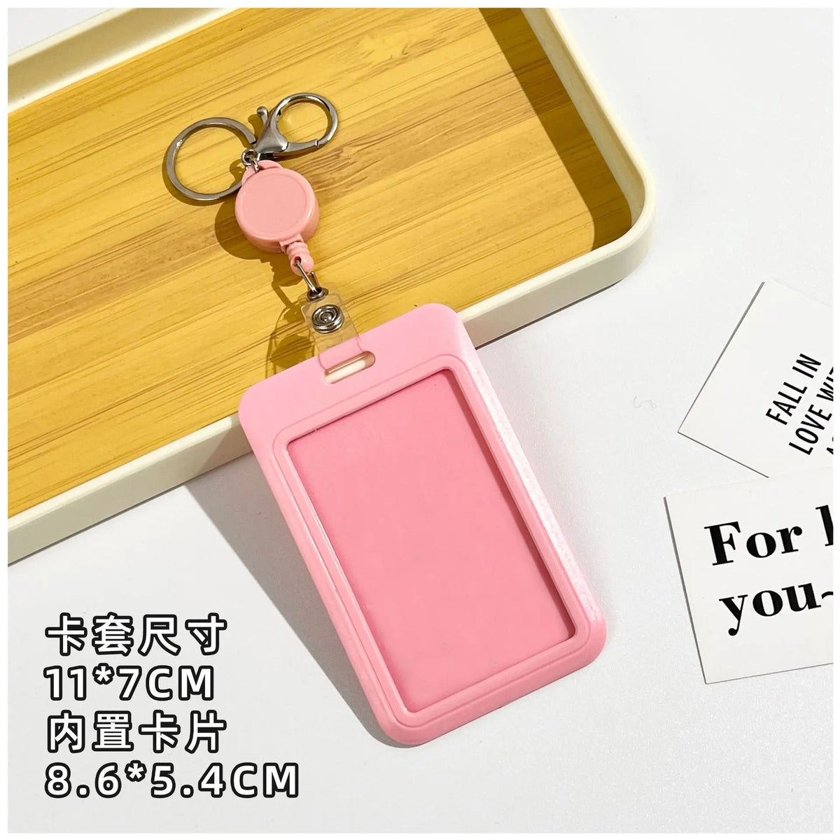 A pink rectangular ID badge holder with a keychain attached, displayed on a wooden tray.