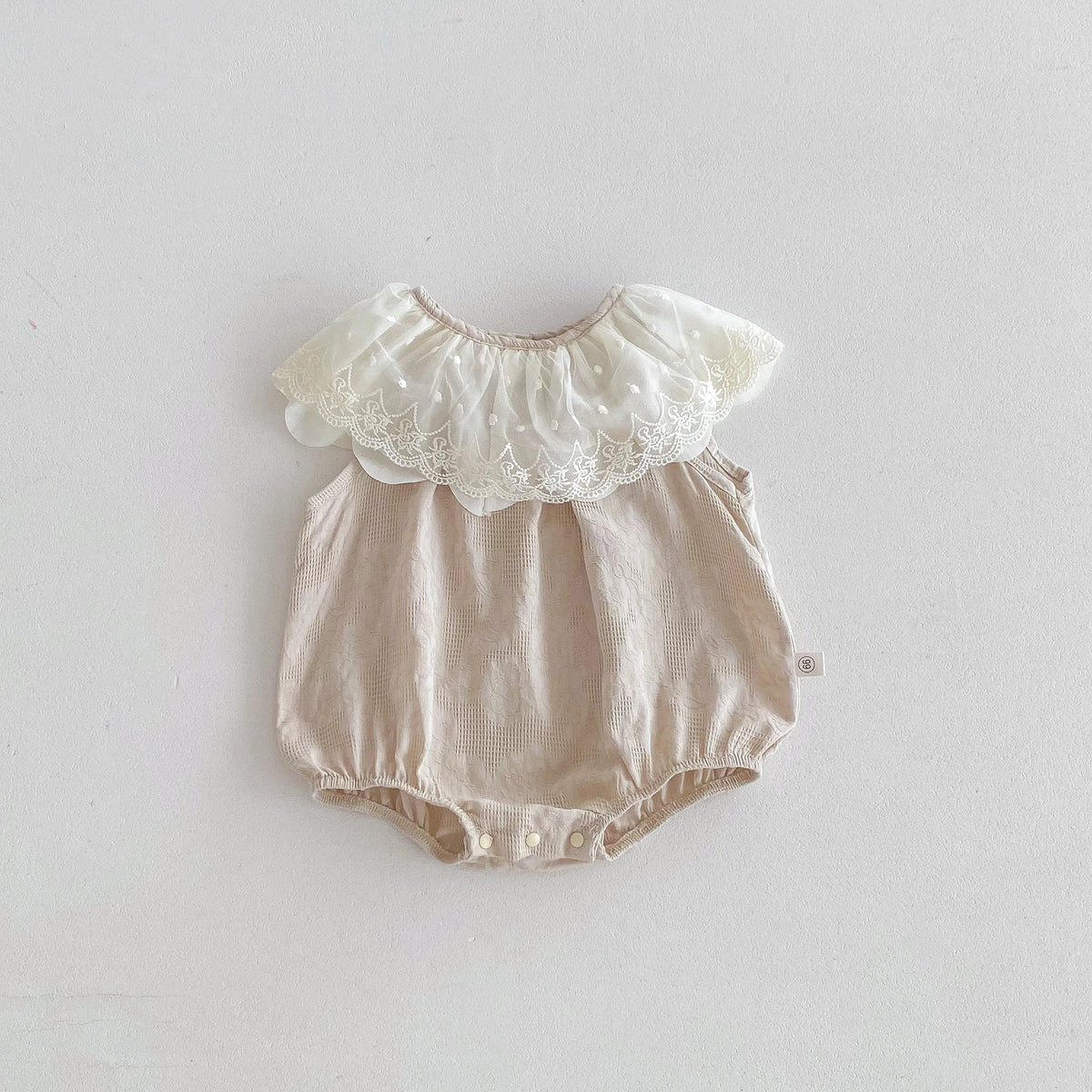 A beige baby girl sleeveless jumpsuit with a white lace collar and gathered fabric details.