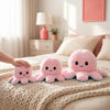 Pink and blue double-sided flip octopus plush toys resting on a beige blanket.