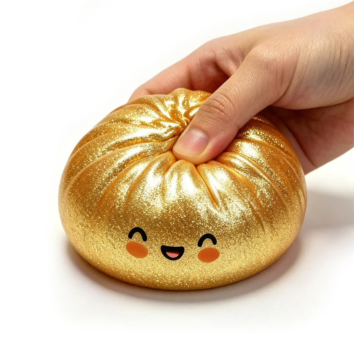 Une main serre un jouet anti-stress en forme de dumpling pailleté doré avec un visage joyeux.