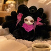 A black nine-tailed fox plush collectible with pink accents resting on white fabric next to an open book.