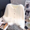 A white faux fur cardigan sweater draped on a hanger against a dark background.
