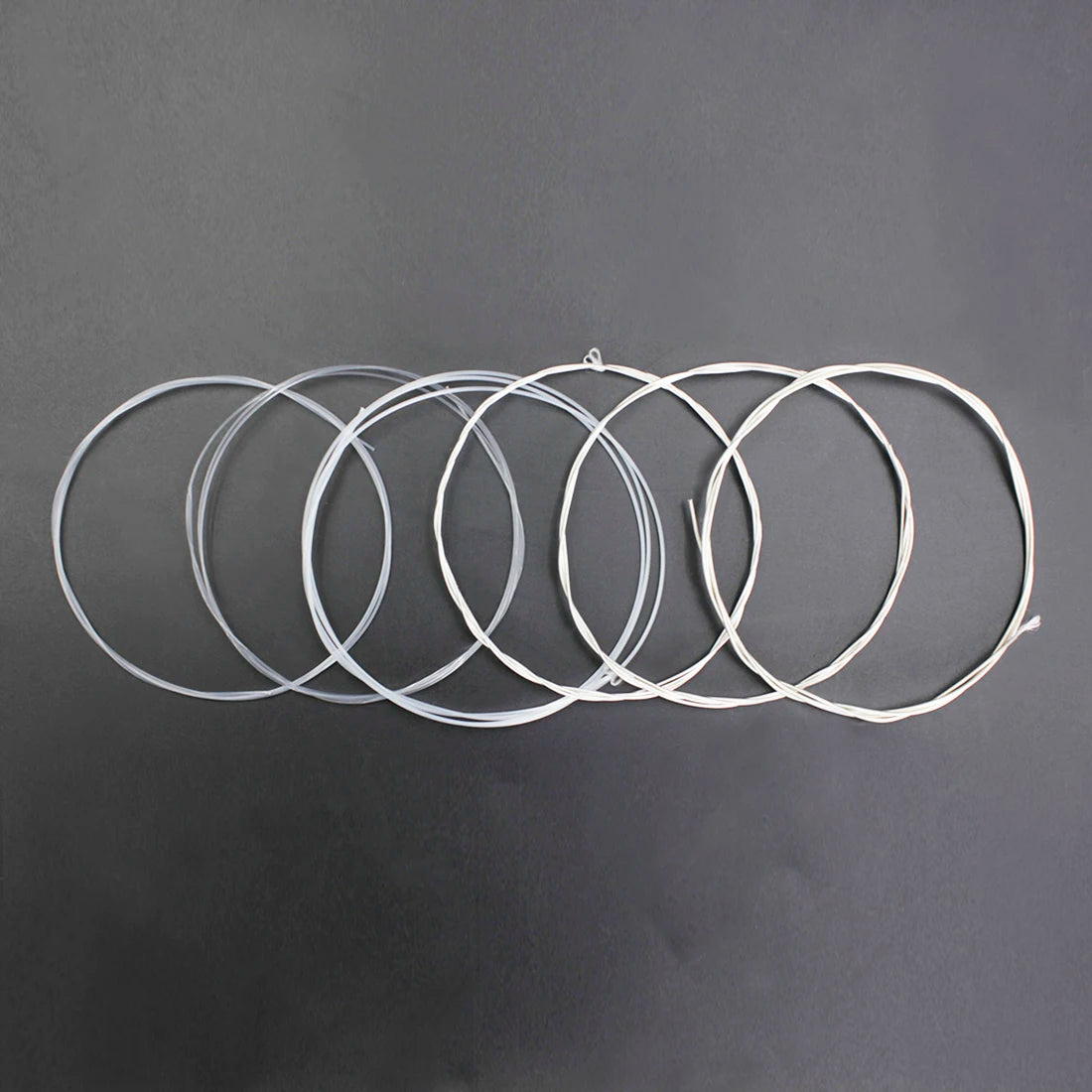 A collection of silver-plated classical guitar strings with transparent nylon cores arranged in a line.