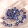 A cluster of iridescent purple and blue acrylic four-petal flower beads on a clear slab for jewelry making