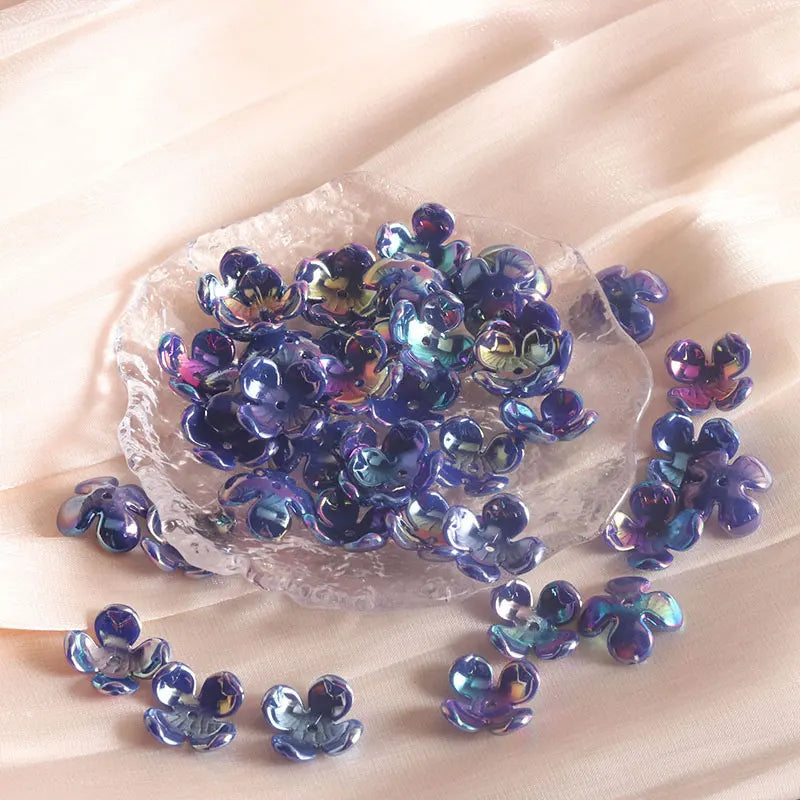 A cluster of iridescent purple and blue acrylic four-petal flower beads on a clear slab for jewelry making