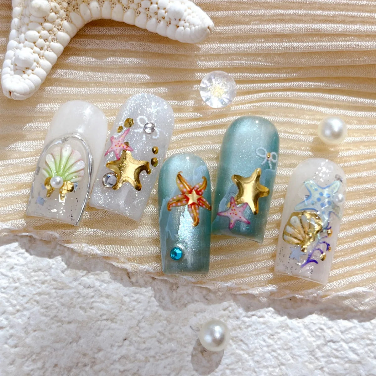 A collection of 3D ocean-themed nail art stickers featuring gold shells and starfish on clear and blue nails.
