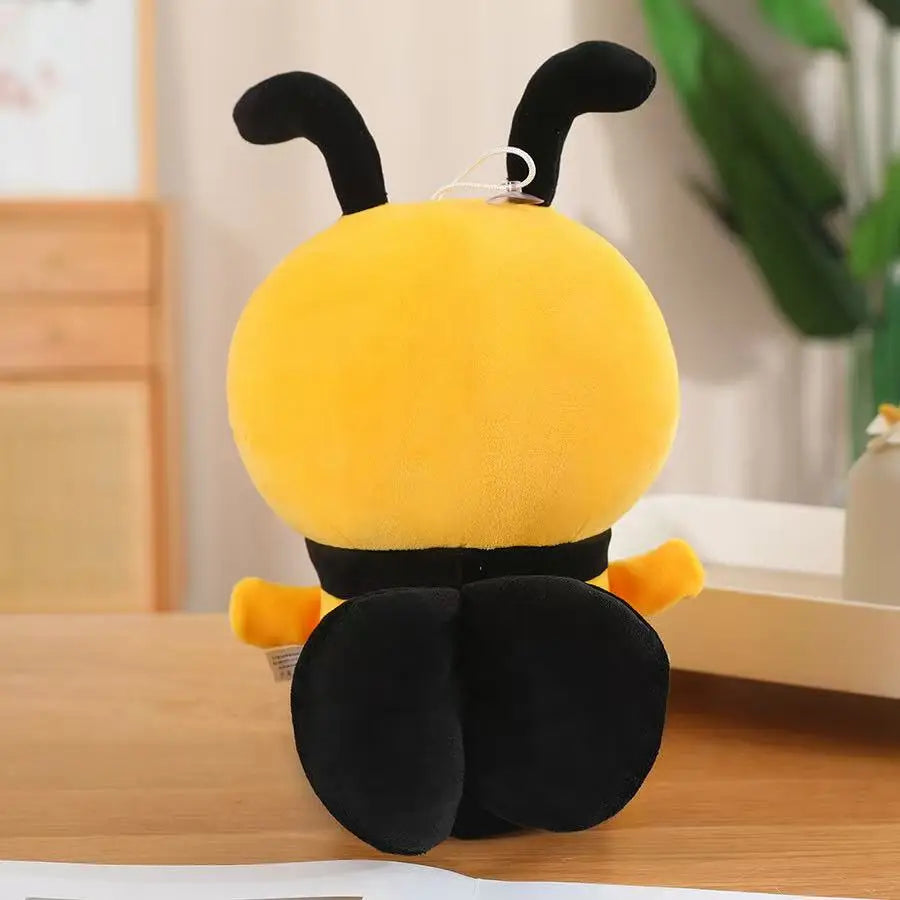 A yellow and black handmade bee plush pillow with large ears sitting on a wooden surface.