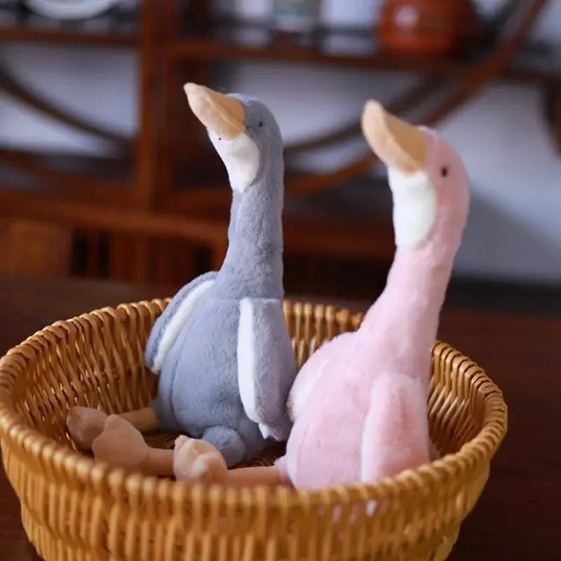 A pair of soft plush toys resembling long-necked geese in gray and pink colors sitting in a woven basket.