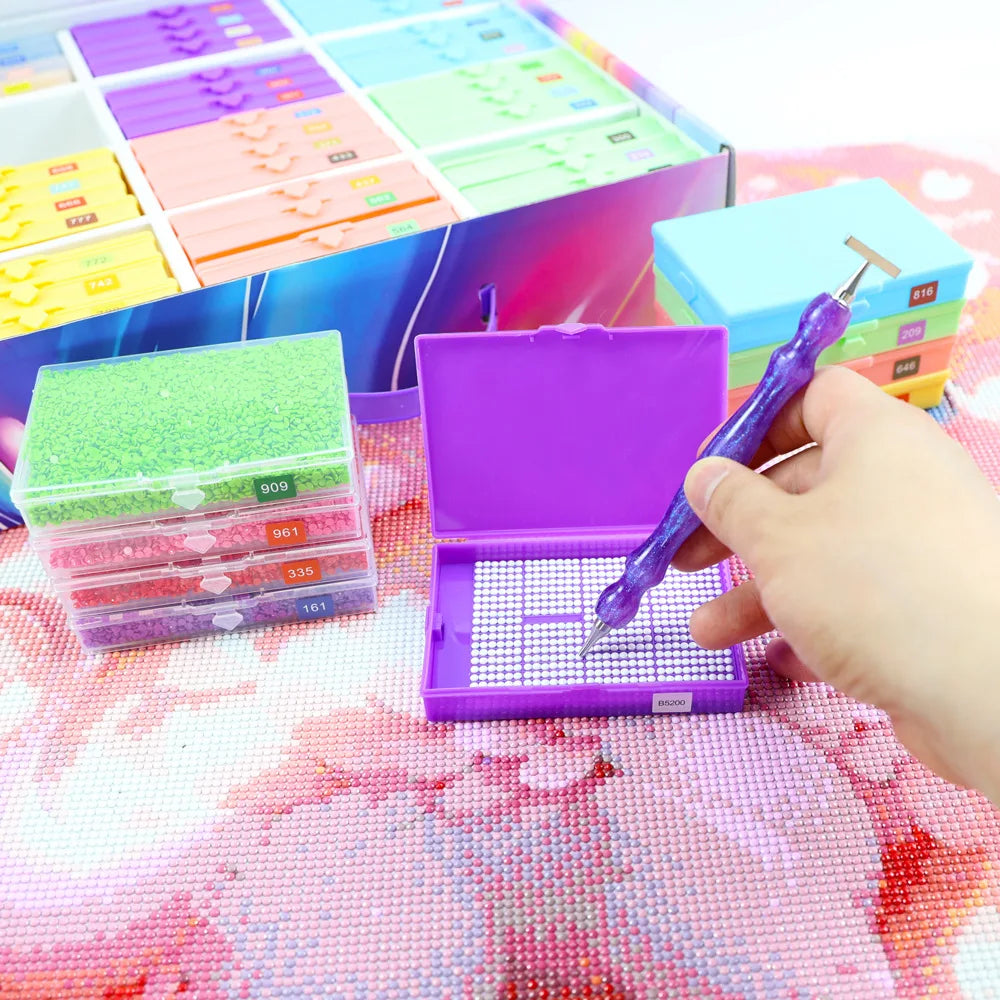A hand is opening a purple diamond painting storage organizer box, revealing a tray of colored sequins and beads.