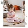 A toddler is sitting on the floor wearing a pink cotton sleeping bag or sack.