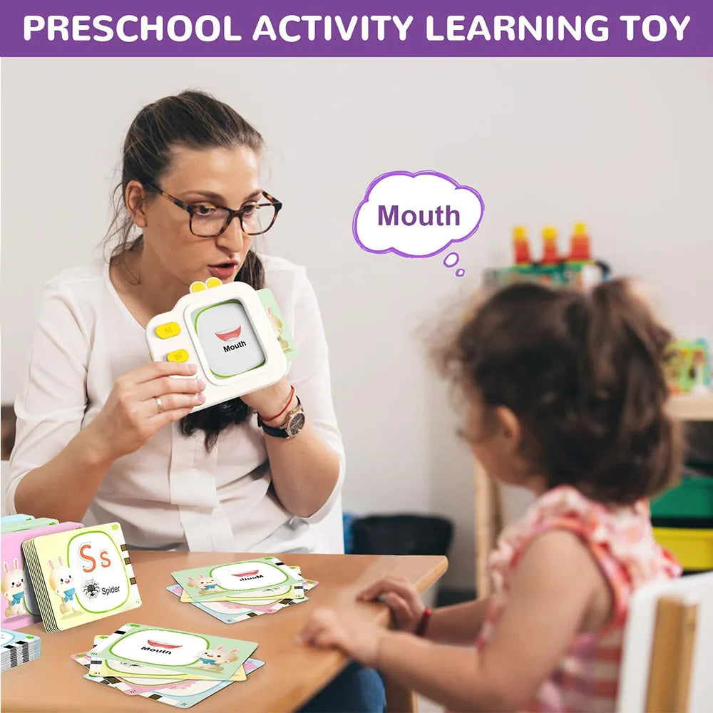 A woman demonstrates an interactive learning toy flash card to a young child in a classroom setting.