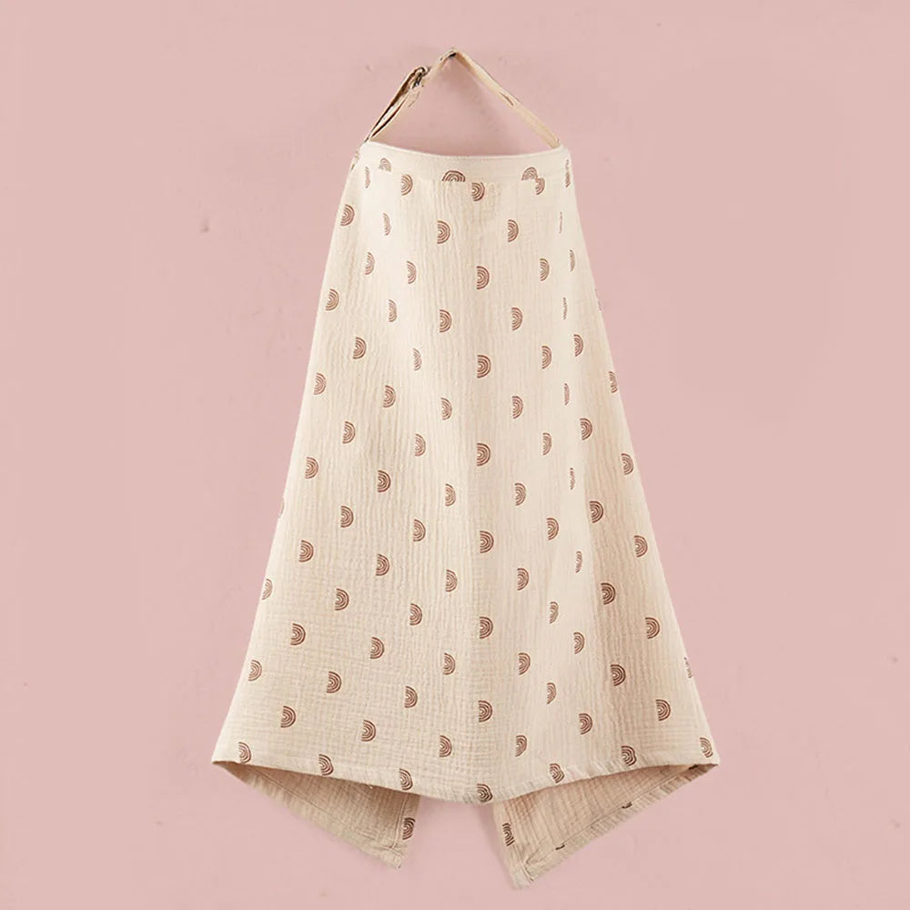 A cream-colored breathable muslin nursing cover with a dotted pattern is displayed against a pink background.