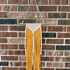 A hanging display of natural wooden spacer beads in yellow and white thread against a brick wall.
