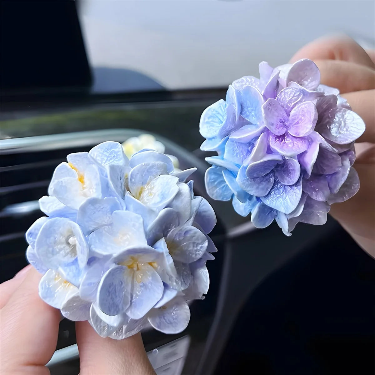 A hand holds a cluster of light blue and purple silicone flower blossoms used for crafts and candles.