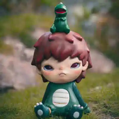 A small mischievous figure with reddish-brown hair and green skin is shown sitting in a grassy outdoor setting.