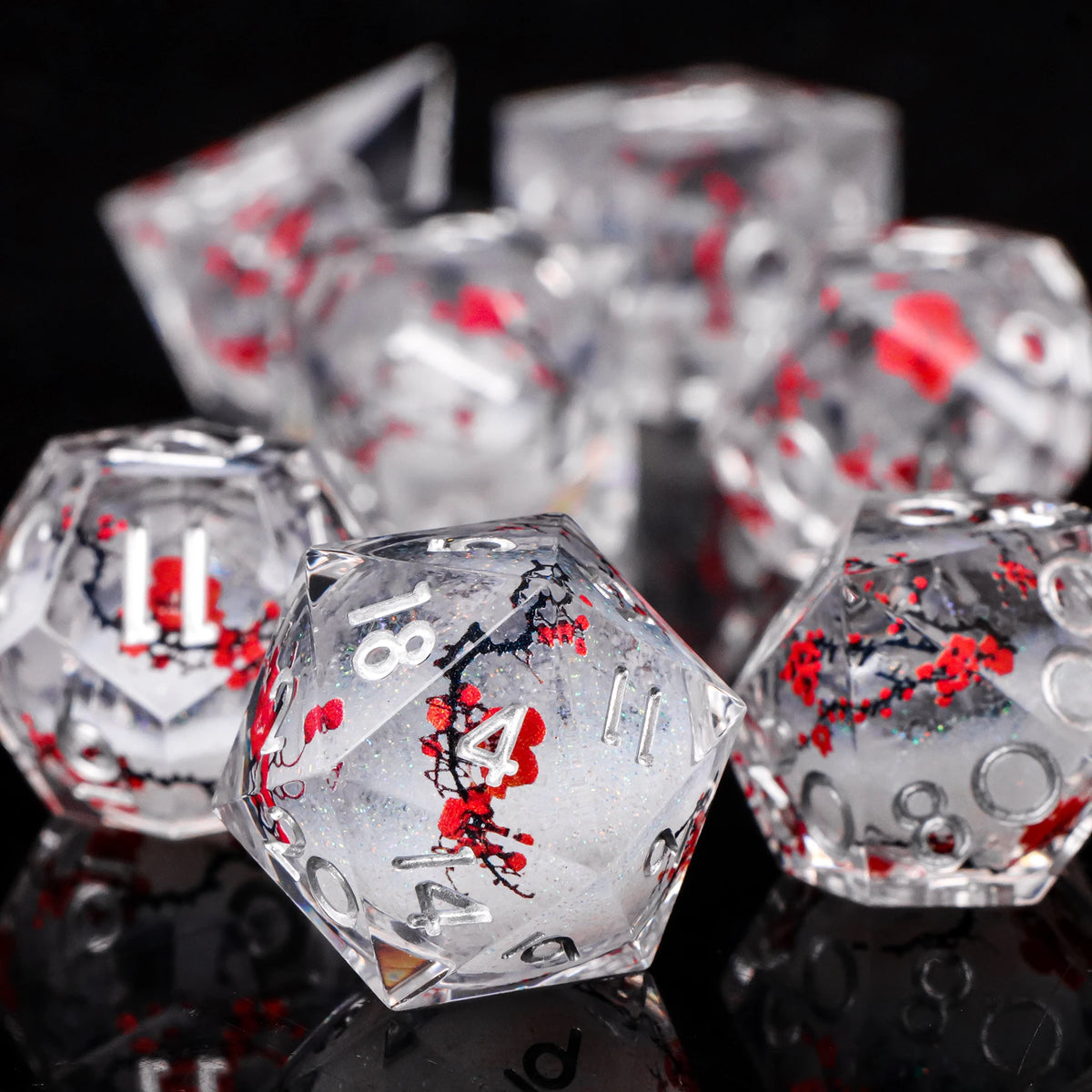 A close-up of a set of clear resin dice with red plum blossom designs, reflecting on a dark surface.