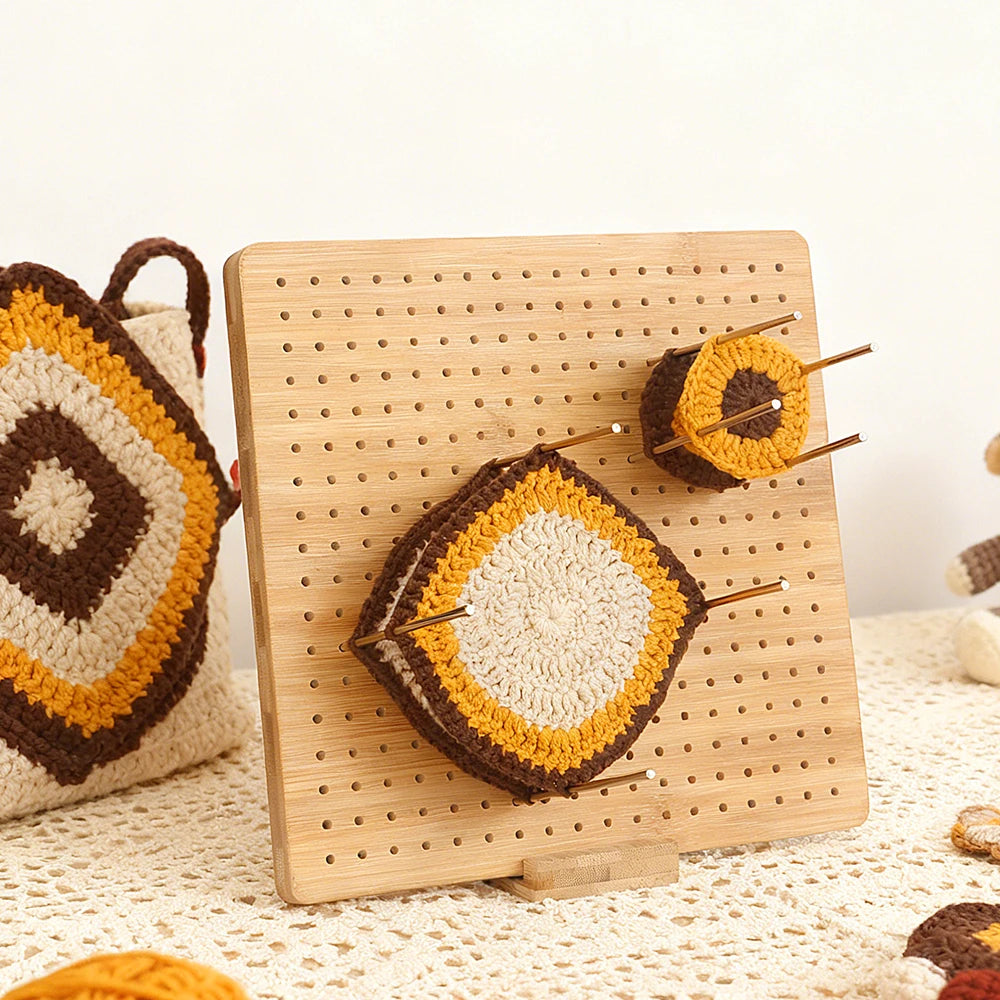 A wooden bamboo crochet blocking board with pins and stand displaying a finished crocheted item.