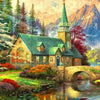 A picturesque forest house with a steeple and stone bridge over a stream, surrounded by lush greenery and mountains.