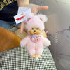 A pink fluffy bear plush toy with a yellow nose and pink accents is held by a hand against a black and white patterned fabric