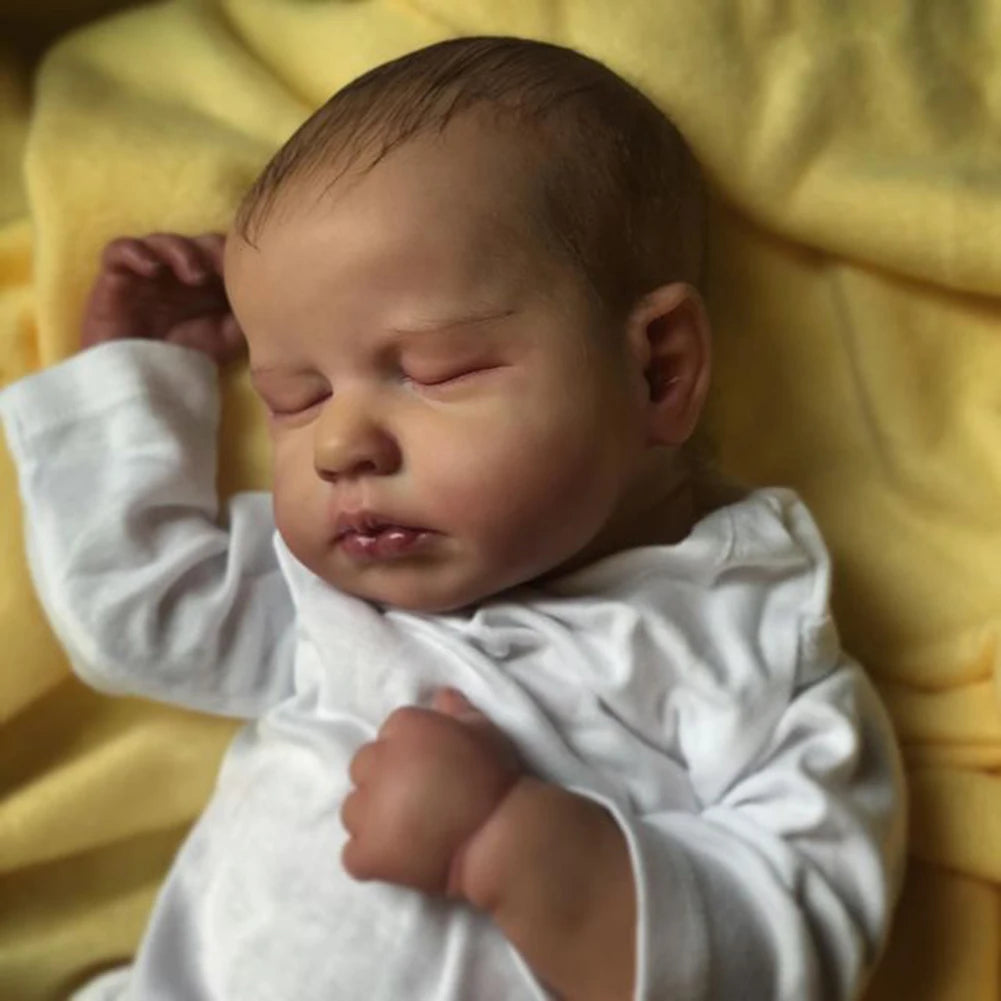 A newborn baby doll with a cloth body is lying on yellow fabric.