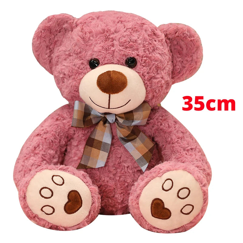 A pink teddy bear plush pillow with a brown nose and a plaid bow.
