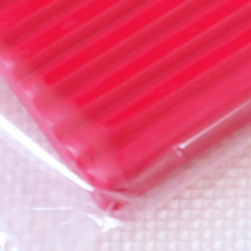 A close-up view of a bright pink polymer clay kit with a ribbed texture, packaged in clear plastic.