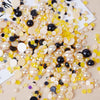A scatter of mixed resin rhinestone pearls in yellow, cream, and black finishes for crafts and nail art.