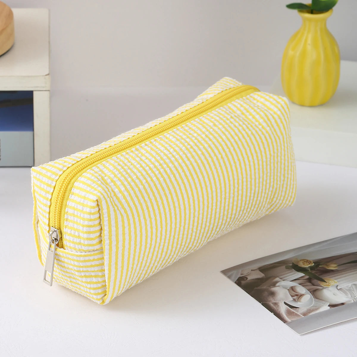 A yellow and white striped canvas pencil case with a zipper is shown on a white surface.