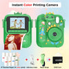 A green instant color printing camera with a dinosaur-themed design, showing examples of printed photos and accessories.