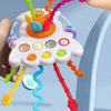 A hand is pulling a colorful string toy with various shapes and colors from a cloud-like structure for a baby's sensory exerc