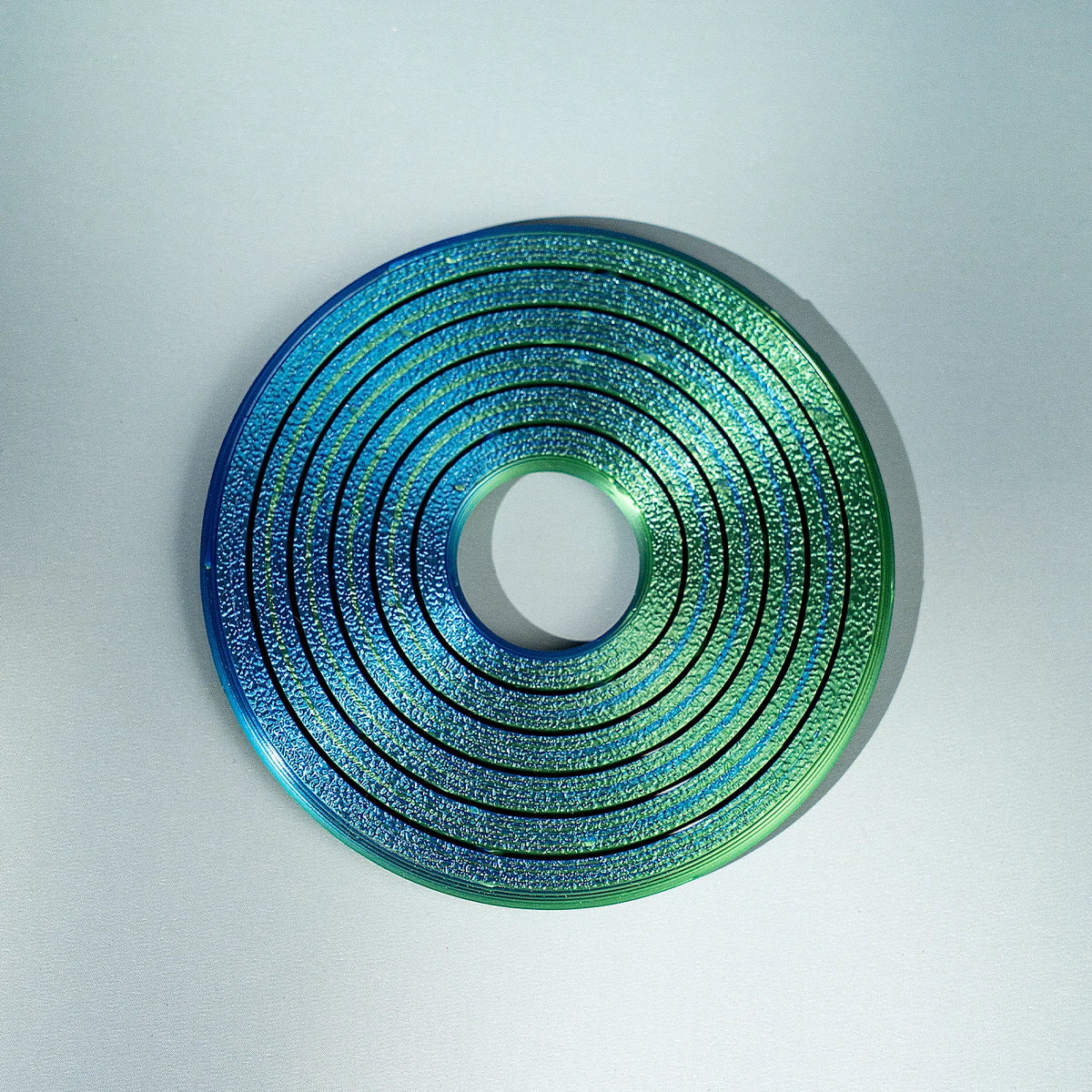 A circular, iridescent spinner ring with concentric grooves in shades of blue and green.