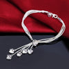 Elegant sterling silver snake chain bracelet with small heart charms displayed on a dark background.