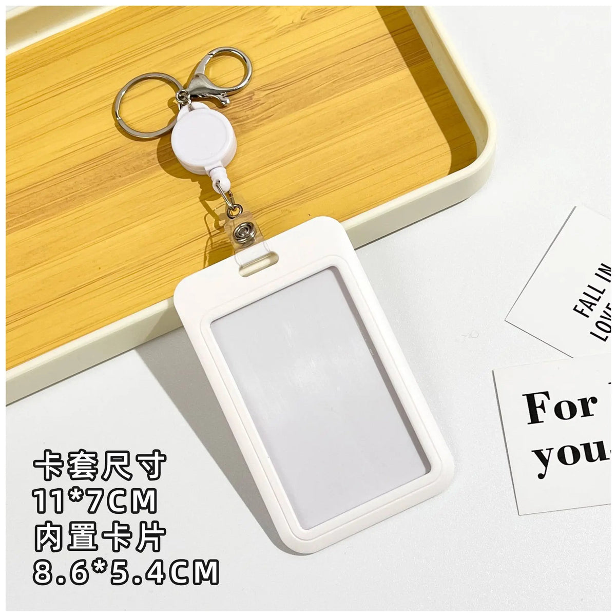 A white rectangular ID badge holder with a clear window is shown next to a keychain and on a wooden tray.