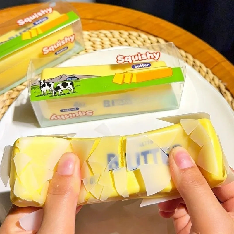 Hands hold a yellow squishy butter bar stress relief toy next to other squishy bars.