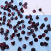 A close-up view of dark red glass beads resembling Lily of the Valley flowers scattered on a white surface.