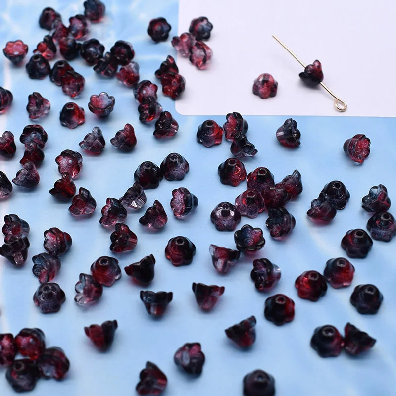 A close-up view of dark red glass beads resembling Lily of the Valley flowers scattered on a white surface.