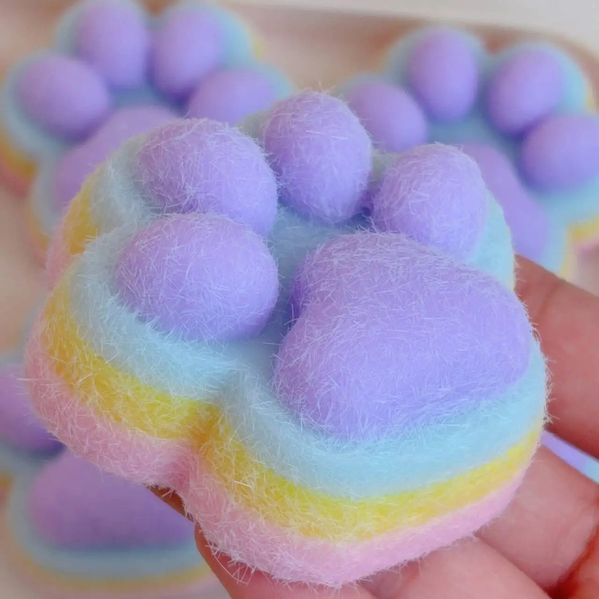 A hand holds a soft, purple and pink cat paw shaped squishy fidget toy.
