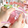 A hand is squeezing a large, pink strawberry squishy stress ball with a green cap for sensory relief.