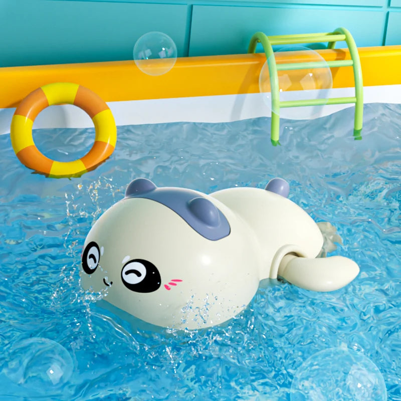 A white and gray clockwork animal bath toy floats in blue water with a yellow ring and green rack visible.