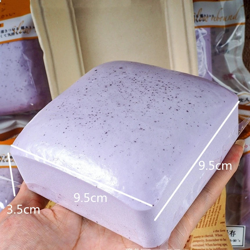 A purple squishy stress relief toy shaped like a square block is held in a hand.